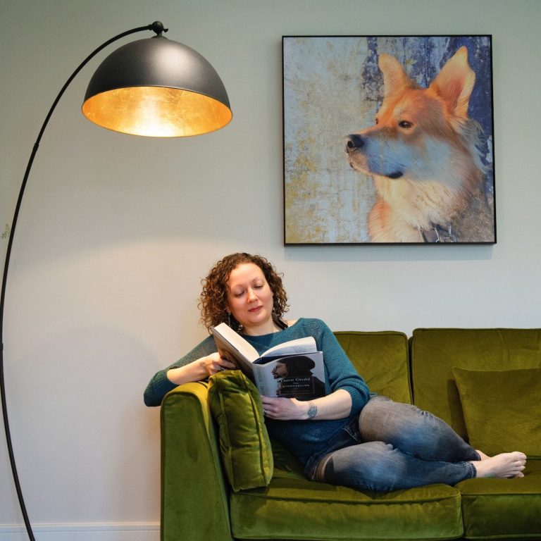 Marvellous Marvin's Fur Baby Art A woman reading on a green sofa, with a lamp and a dog painting on the wall.
